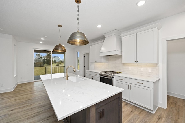 kitchen featuring stainless steel range, custom range hood, white cabinets, and sink