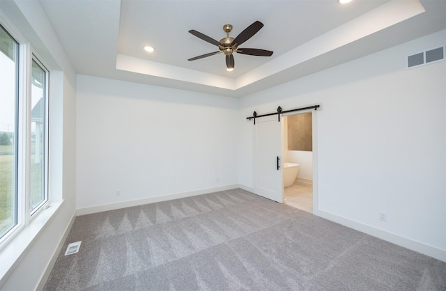 carpeted empty room featuring ceiling fan, a barn door, and a tray ceiling