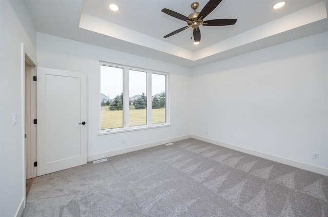 carpeted empty room featuring ceiling fan and a raised ceiling