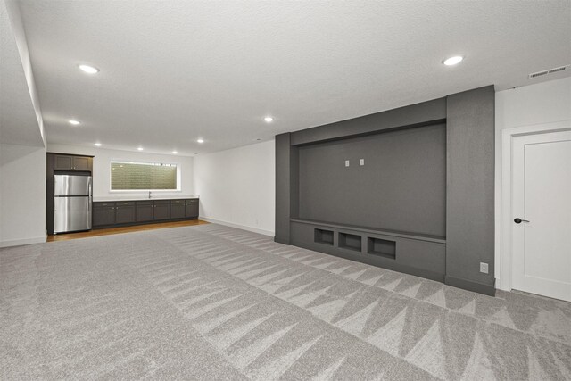 basement with carpet, a textured ceiling, and stainless steel refrigerator