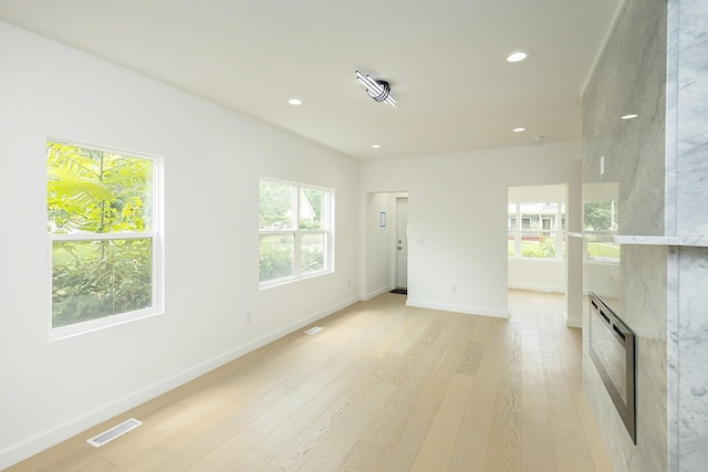 unfurnished room featuring heating unit, a healthy amount of sunlight, a fireplace, and light hardwood / wood-style flooring