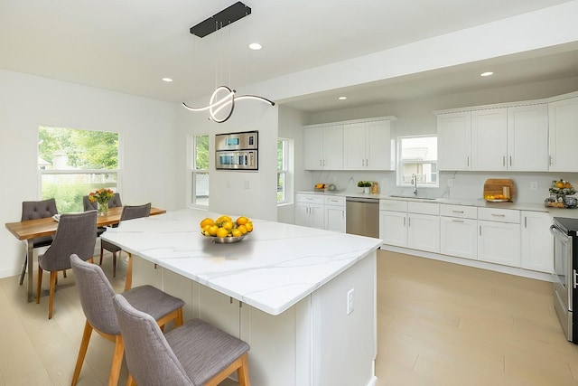 kitchen featuring sink, appliances with stainless steel finishes, white cabinetry, hanging light fixtures, and a center island