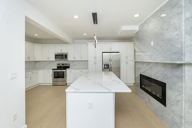 kitchen with light stone counters, stainless steel appliances, a center island, and white cabinets