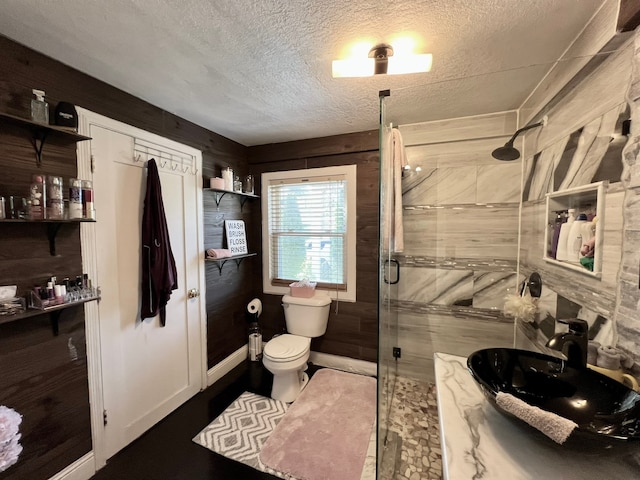 bathroom with a textured ceiling, sink, wooden walls, walk in shower, and toilet