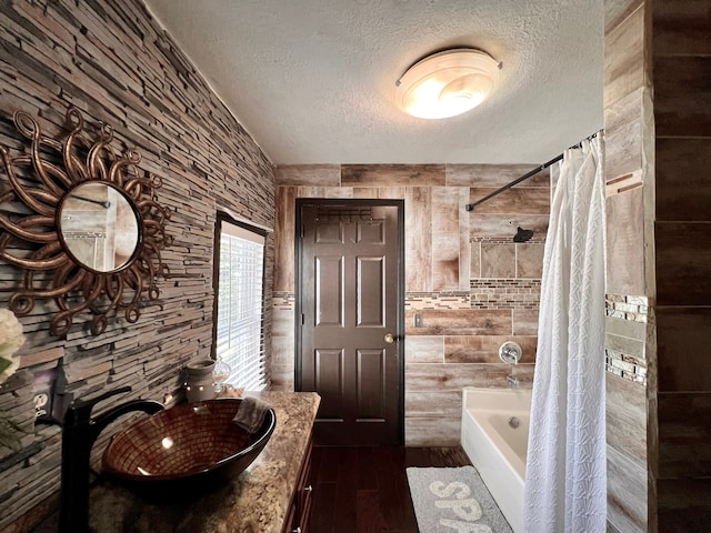 bathroom featuring vanity, wood walls, a textured ceiling, hardwood / wood-style floors, and shower / tub combo with curtain