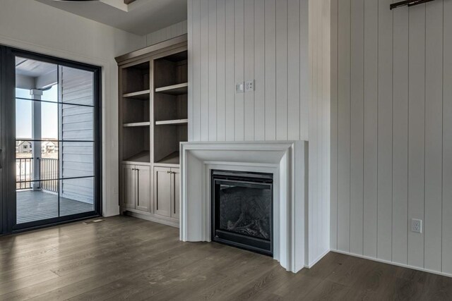 unfurnished living room featuring built in shelves, dark hardwood / wood-style flooring, and wood walls