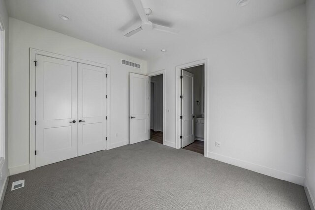 unfurnished bedroom with ceiling fan, a closet, dark carpet, and ensuite bath