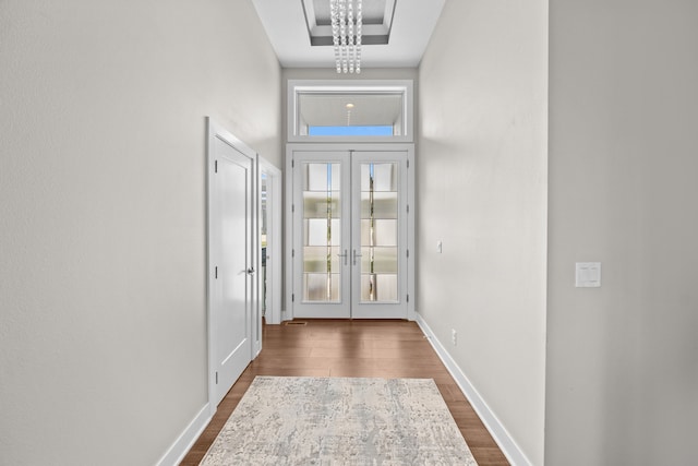 doorway to outside featuring dark wood-type flooring, an inviting chandelier, a towering ceiling, and french doors