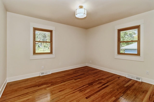 spare room with wood finished floors, visible vents, and plenty of natural light