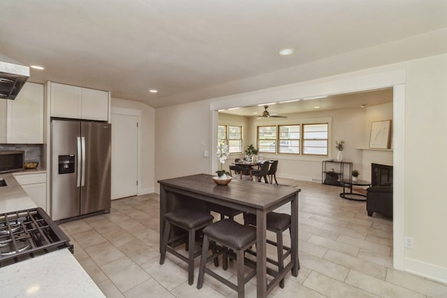 interior space featuring ceiling fan, white cabinets, tasteful backsplash, a brick fireplace, and appliances with stainless steel finishes