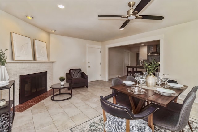 dining room with a brick fireplace, ceiling fan, and light tile patterned floors