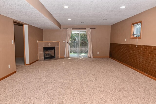 unfurnished living room with carpet, a textured ceiling, a tile fireplace, and brick wall