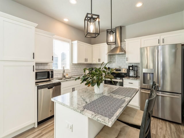 kitchen with a center island, wall chimney range hood, sink, appliances with stainless steel finishes, and light stone counters