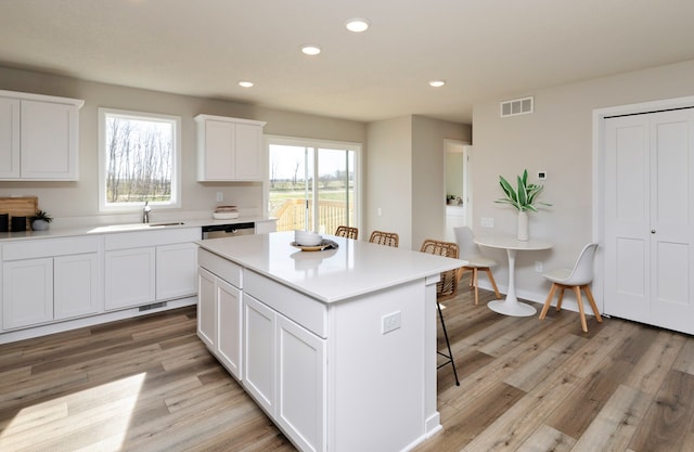 kitchen featuring light hardwood / wood-style floors, a center island, sink, a breakfast bar area, and white cabinets