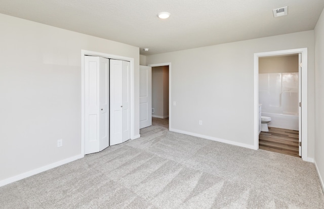 unfurnished bedroom with light carpet, a closet, and ensuite bath