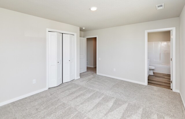 unfurnished bedroom featuring connected bathroom, light carpet, and a closet