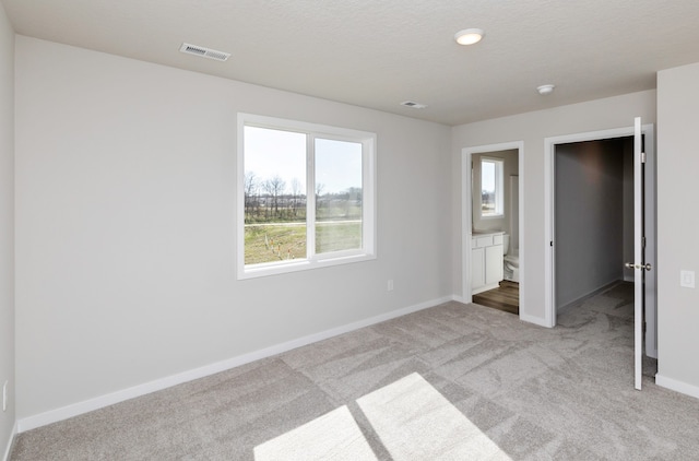 unfurnished bedroom featuring a textured ceiling, ensuite bathroom, and light colored carpet