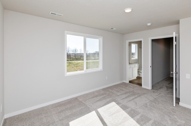 unfurnished bedroom with light carpet, a textured ceiling, and ensuite bathroom