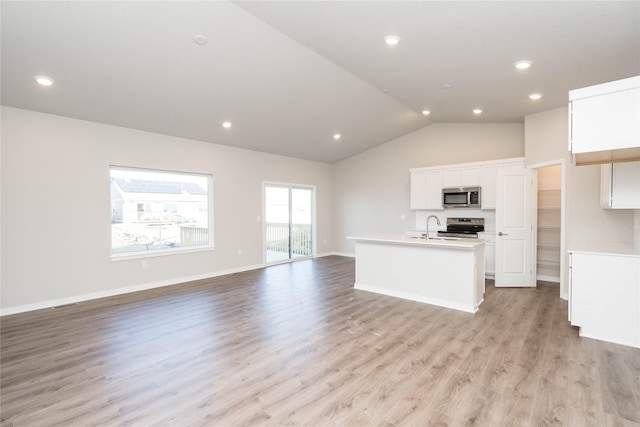 kitchen featuring stainless steel appliances, vaulted ceiling, a center island with sink, white cabinets, and light wood-type flooring