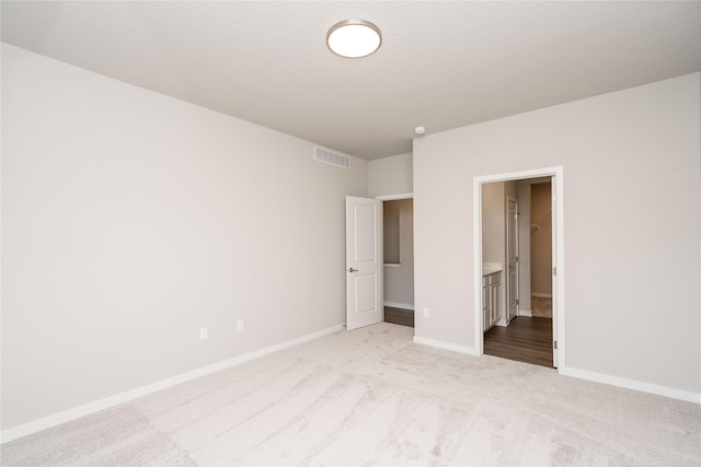 unfurnished bedroom with light carpet, ensuite bathroom, and a textured ceiling