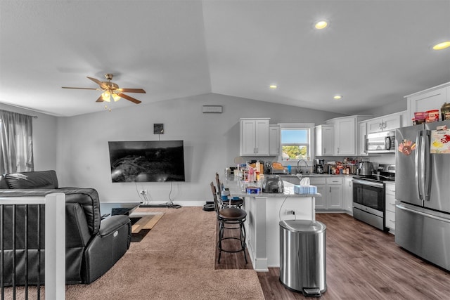 kitchen with lofted ceiling, white cabinetry, appliances with stainless steel finishes, dark hardwood / wood-style floors, and a breakfast bar