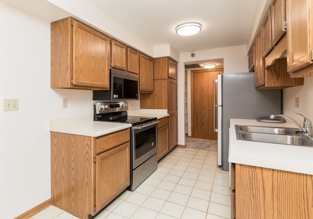 kitchen with appliances with stainless steel finishes, a textured ceiling, sink, and light tile patterned floors