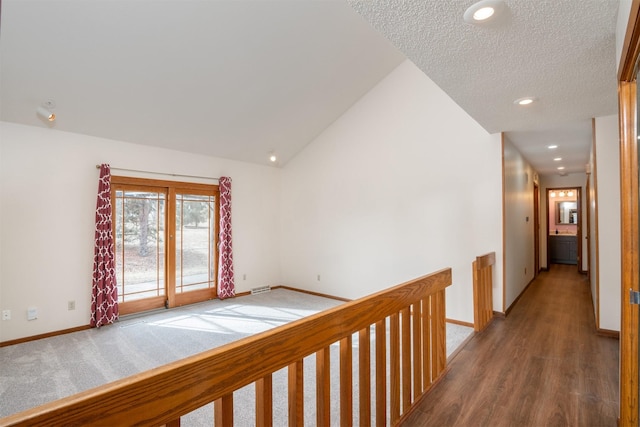 hallway with lofted ceiling, hardwood / wood-style floors, and a textured ceiling