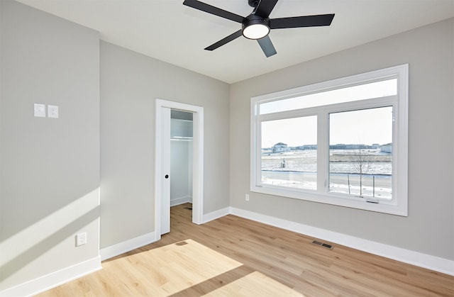 unfurnished bedroom featuring ceiling fan, light hardwood / wood-style floors, a walk in closet, and a closet