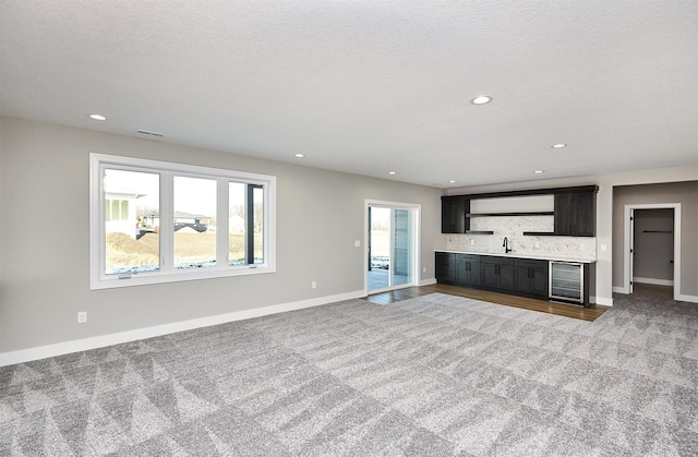 unfurnished living room with a healthy amount of sunlight, sink, beverage cooler, and light carpet