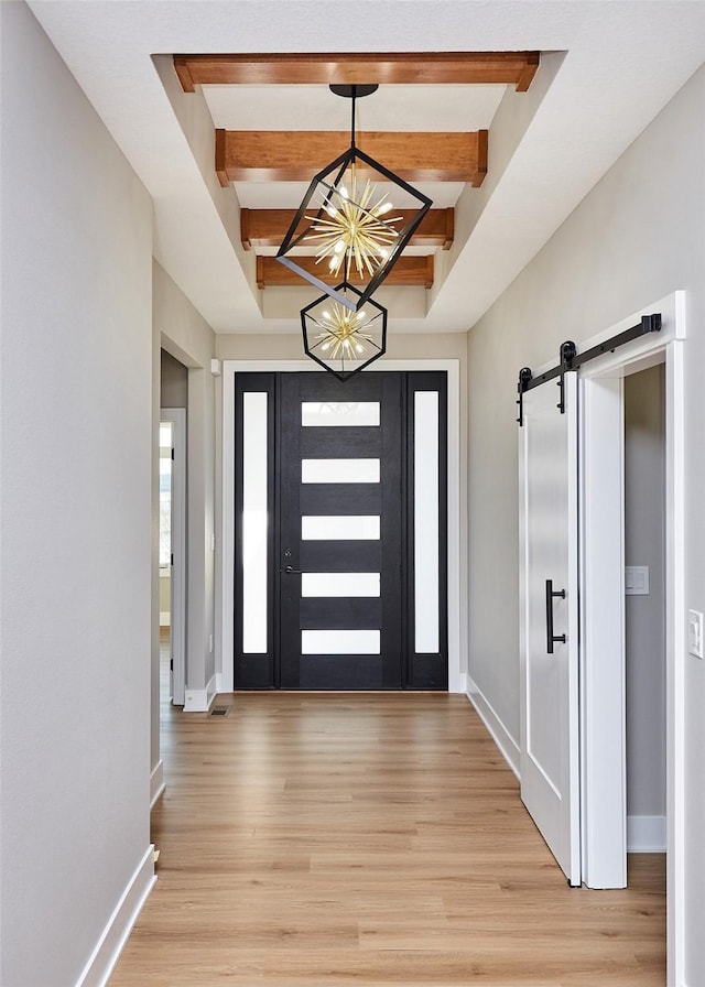 entryway featuring beamed ceiling, a barn door, light hardwood / wood-style flooring, and a chandelier