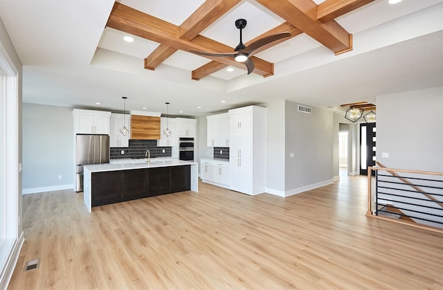 kitchen with a kitchen island with sink, coffered ceiling, white cabinets, sink, and hanging light fixtures