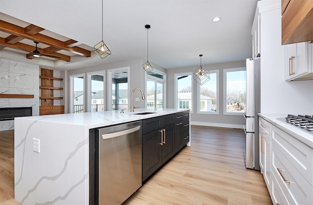 kitchen with sink, beamed ceiling, an island with sink, white cabinets, and appliances with stainless steel finishes