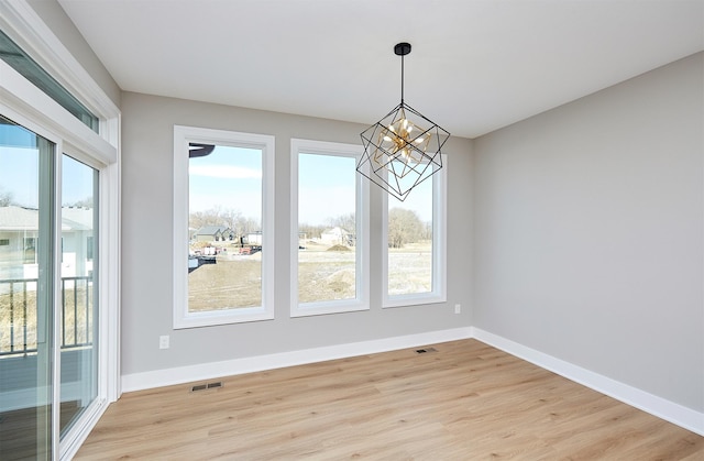 unfurnished dining area with a healthy amount of sunlight, a chandelier, and light wood-type flooring