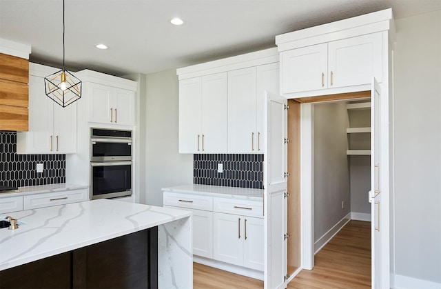 kitchen with white cabinetry, light stone countertops, tasteful backsplash, double oven, and pendant lighting