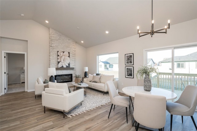 living room featuring a chandelier, a stone fireplace, high vaulted ceiling, and light hardwood / wood-style flooring