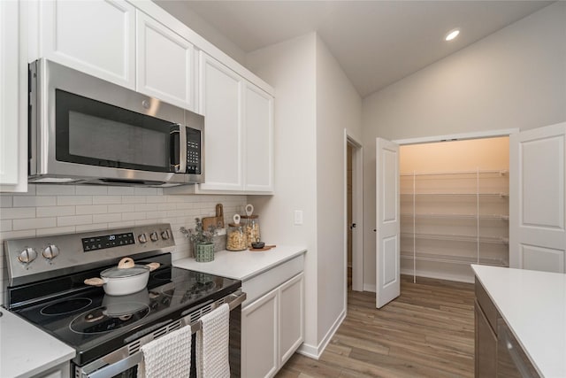 kitchen featuring white cabinetry, stainless steel appliances, backsplash, light hardwood / wood-style floors, and lofted ceiling