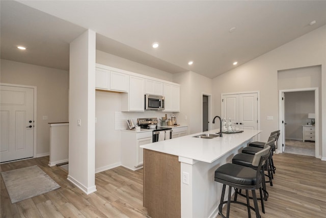 kitchen featuring stainless steel appliances, a kitchen island with sink, sink, white cabinets, and a breakfast bar area