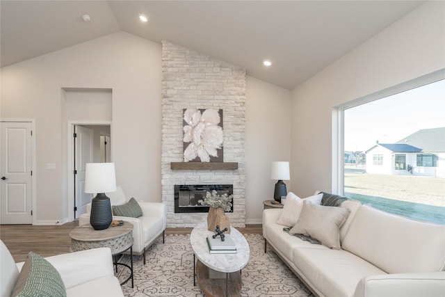 living room with a stone fireplace, light hardwood / wood-style floors, and vaulted ceiling