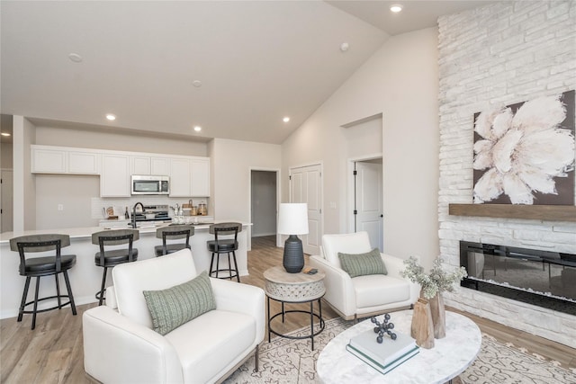 living room featuring light hardwood / wood-style floors, sink, a fireplace, and high vaulted ceiling