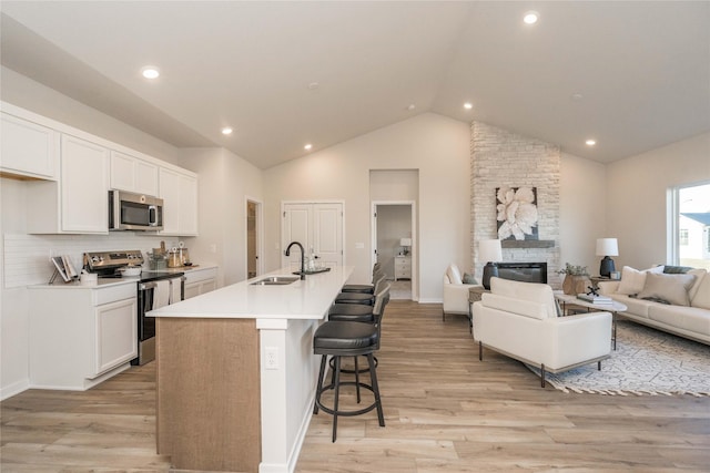 kitchen with a kitchen island with sink, sink, appliances with stainless steel finishes, light hardwood / wood-style floors, and white cabinetry