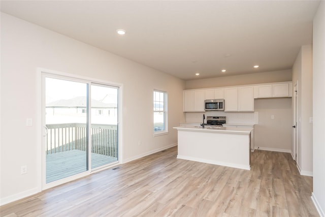 kitchen featuring a kitchen island with sink, white cabinets, light wood-type flooring, and appliances with stainless steel finishes