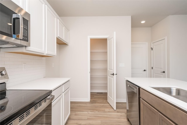 kitchen featuring stainless steel appliances, white cabinetry, tasteful backsplash, and light hardwood / wood-style floors