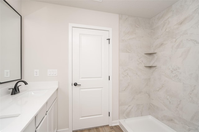 bathroom with wood-type flooring, vanity, and a tile shower