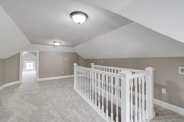 additional living space with a textured ceiling, light colored carpet, and lofted ceiling