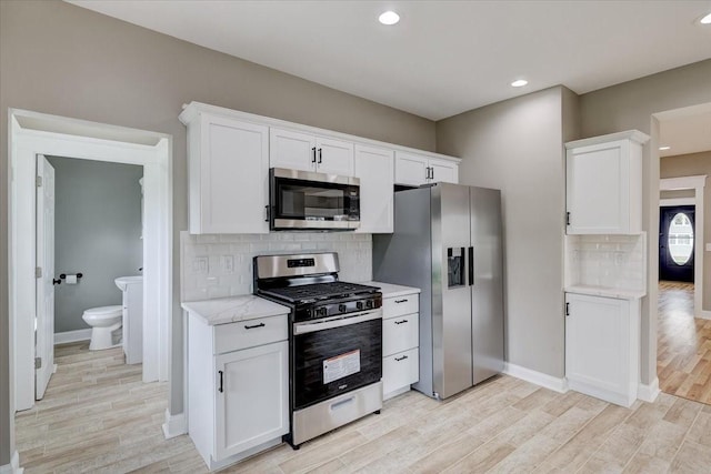 kitchen with light stone countertops, appliances with stainless steel finishes, light wood-type flooring, and white cabinetry