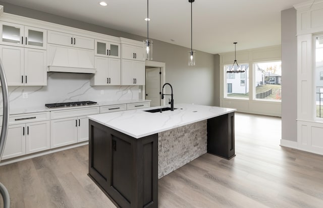 kitchen with premium range hood, a kitchen island with sink, and white cabinetry