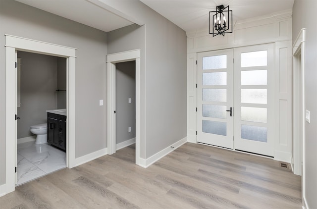 foyer with french doors, light hardwood / wood-style floors, and a chandelier