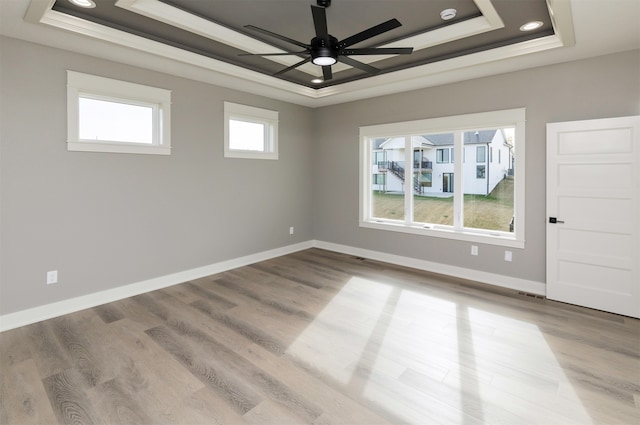 empty room featuring a tray ceiling, light hardwood / wood-style floors, and ceiling fan