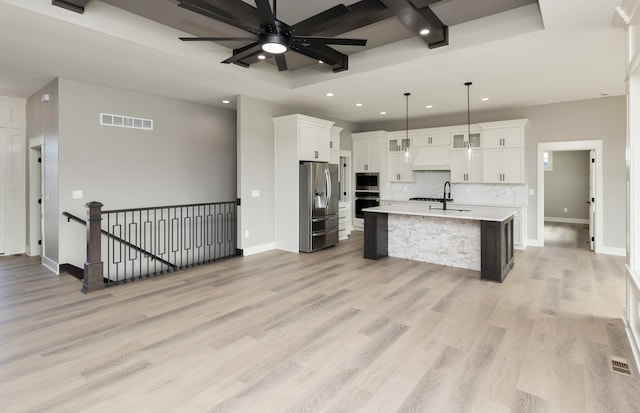 kitchen featuring appliances with stainless steel finishes, backsplash, white cabinetry, decorative light fixtures, and a kitchen island with sink