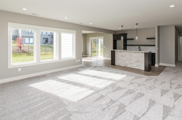 unfurnished living room featuring a healthy amount of sunlight, carpet, and sink